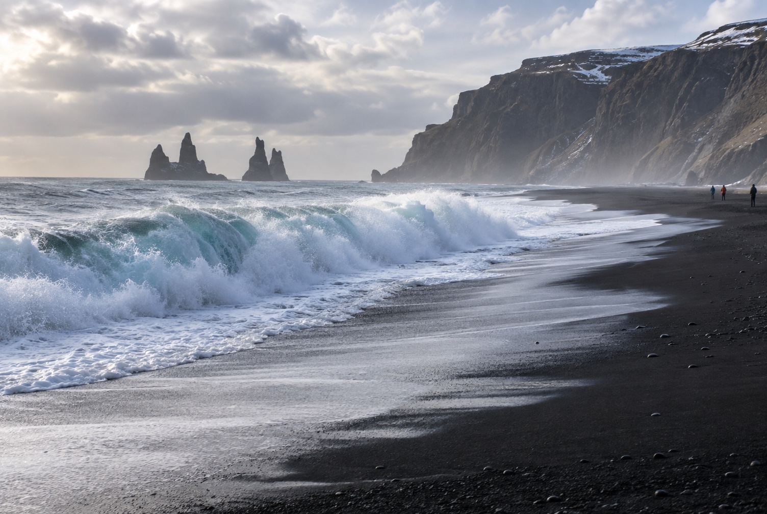 Wave run-up crossing the black sand at Reynisfjara with visitors kept well back