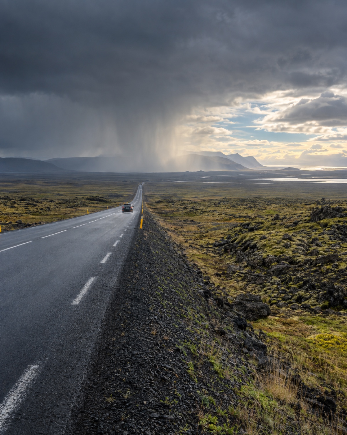 Route 1 crossing an open moss-and-lava plain under a visible rain shaft with clearing sky beyond